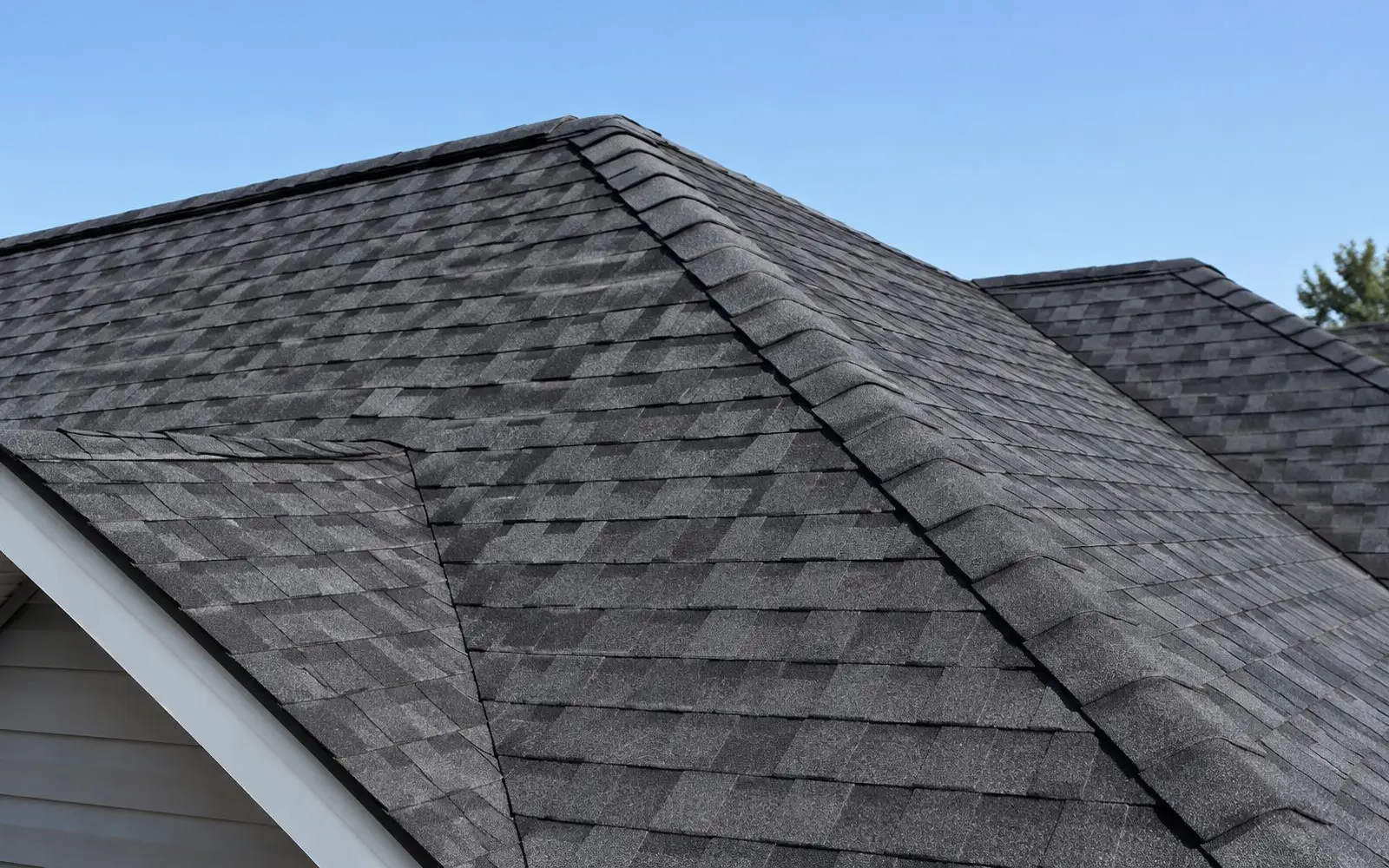 Close view of a residential roof with dark architectural asphalt shingles against a blue sky